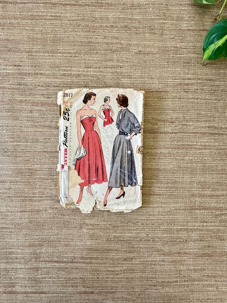 May include: Vintage sewing pattern featuring illustrations of dresses. The pattern packet is off-white with the number "2817" and the price "25c" visible. The dresses are in red and gray, with a retro style.
