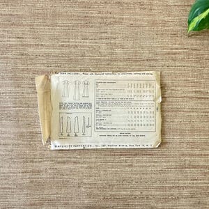May include: Vintage Simplicity sewing pattern on a textured surface. The pattern includes illustrations of dresses and detailed instructions. The pattern is from Simplicity Pattern Co., Inc., located in New York.