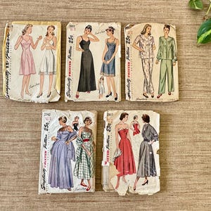 May include: A collection of vintage Simplicity sewing patterns featuring illustrations of dresses, pajamas, and other garments. The patterns are printed on aged paper with the price of 25 cents visible on each. The illustrations depict women in various outfits.