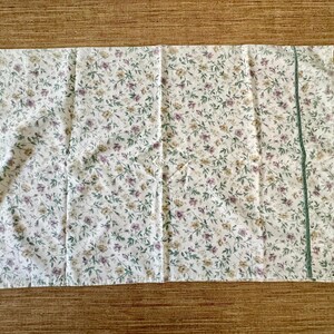 May include: White pillowcase with a floral pattern of small purple, yellow, and green flowers and leaves. A thin green stripe runs vertically along one side. The pillowcase is made of a soft, lightweight fabric.