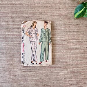 May include: Vintage Simplicity printed pattern for pajamas. The pattern envelope features illustrations of pajama sets, one with floral print pants and the other in solid green. The envelope reads "Simplicity Printed Pattern" and "25&cent;".