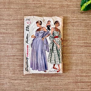 May include: Vintage Simplicity printed sewing pattern 2742. The pattern features illustrations of women's dresses, including a long, light purple gown and a plaid dress with a red belt. The pattern is marked "25c" and "Size 16".