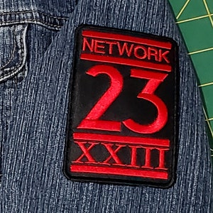 Pode incluir: Uma jaqueta de ganga preta com um remendo bordado em vermelho e preto que diz "NETWORK 23 XXIII".