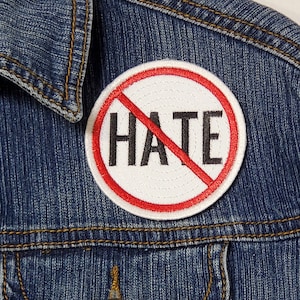 Könnte beinhalten: Eine blaue Jeansjacke mit einem roten Kreis-Patch, auf dem "NO HATE" mit einem roten Strich durch das Wort "hate" steht.