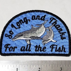Könnte beinhalten: Ein blauer und schwarzer gestickter Aufnäher mit einer Delfin-Familie und dem Text "So Long and Thanks for all the Fish".