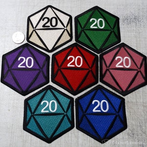Può includere: Sette toppe a forma di dado a 20 facce in diversi colori, tra cui viola, rosso, rosa, verde, bianco, blu e blu-verde. Ogni toppa ha un contorno nero e un numero "20" bianco al centro.