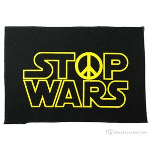 Könnte beinhalten: Schwarzer Stoff-Patch mit gelbem Text, der "STOP WARS" lautet, mit einem Peace-Zeichen in der Mitte des Wortes "STOP".