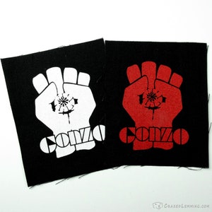 May include: Two black fabric patches with a white fist and the word "GONZO" in white on one patch and a red fist and the word "GONZO" in red on the other patch.