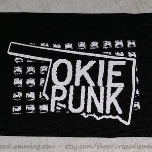 May include: Black and white embroidered patch with the text "OKIE PUNK" inside the outline of the state of Oklahoma.