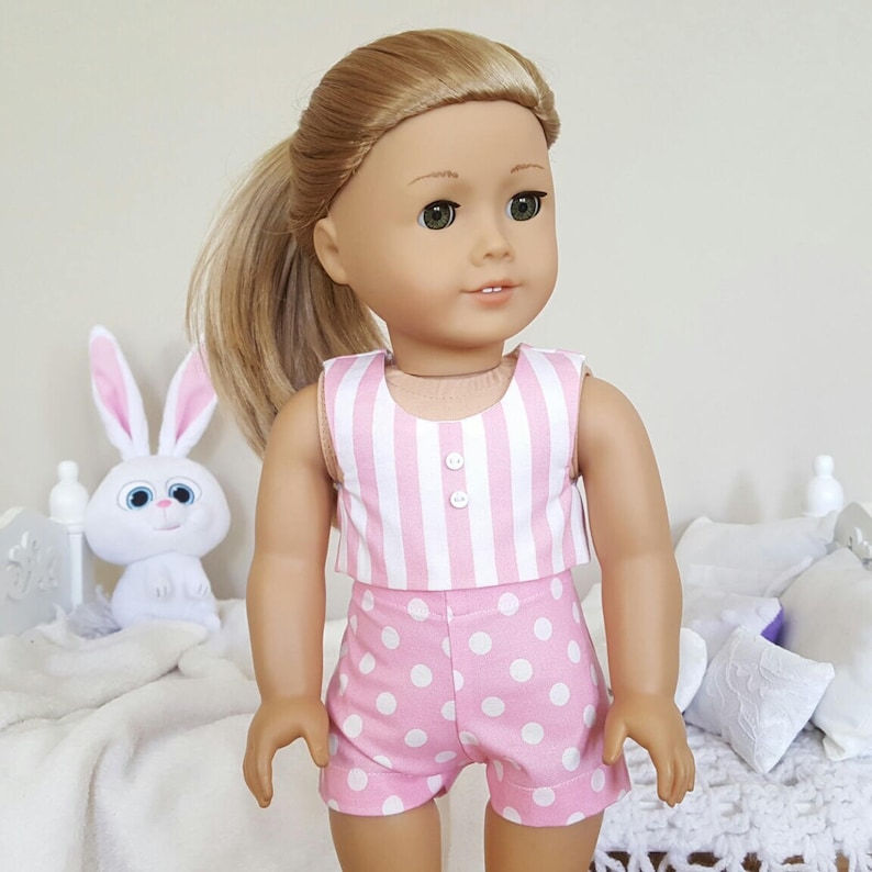 May include: A pink and white striped sleeveless top with white buttons and matching pink and white polka dot shorts. The outfit is designed for a doll.