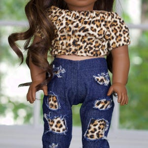 May include: A doll wearing a brown and white leopard print off-the-shoulder top and blue denim jeans with leopard print patches.