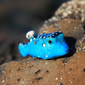 May include: A blue and white ceramic fish figurine with black spots. The fish has a white fin and a large eye.