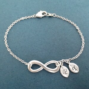 May include: A silver infinity charm bracelet with two small leaf charms with the letters P and N engraved on them.