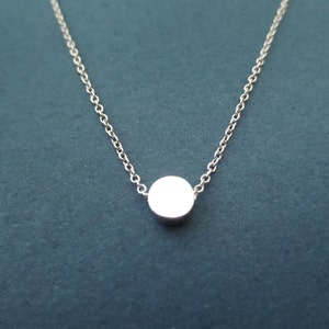 Puede incluir: Un collar de cadena de plata con un pequeño colgante redondo.