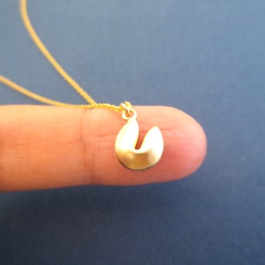 May include: A gold chain necklace with a small gold charm shaped like a fortune cookie.