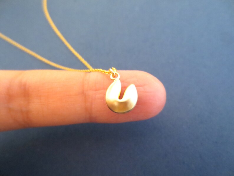 May include: A gold chain necklace with a small gold charm shaped like a fortune cookie.
