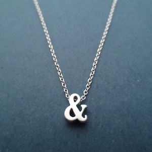 Puede incluir: Un collar de cadena de plata con un pequeño dije de plata en forma de ampersand.