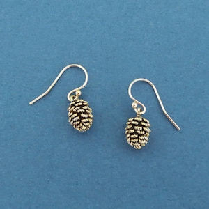 Puede incluir: Un par de pendientes de plata con abalorios de piña de pino dorados. Las piñas de pino son detalladas y realistas.