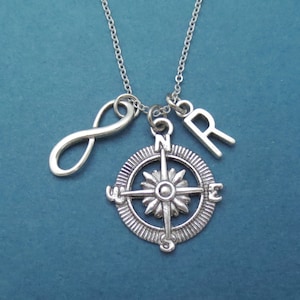 May include: Silver necklace with a compass charm, infinity symbol charm, and letter charms. The compass charm has a flower design in the center.