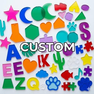 May include: A collection of colorful acrylic shapes, including letters, stars, hearts, and puzzle pieces. The word "CUSTOM" is displayed in white block letters. The shapes are in various colors, such as pink, blue, green, orange, and yellow.