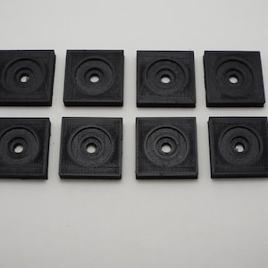 May include: Eight black square-shaped plastic spacers with a circular hole in the center.