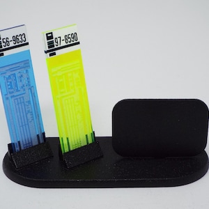 May include: A black desktop organizer with two angled slots holding blue and yellow transparent cards. Each card has a unique number and intricate design. The organizer also has a rectangular slot.