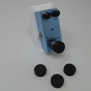 Può includere: Un pedale di chorus analogico blu con tre manopole nere e un supporto in plastica bianca. Il pedale ha la scritta "Analog Chorus" stampata su di esso.