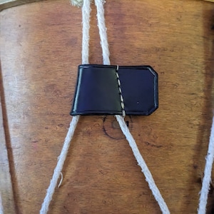 May include: A vintage wooden drum with a red rim and white rope straps. A black leather strap is attached to the rope straps.