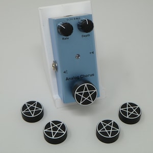 May include: A blue analog chorus pedal with black knobs labeled "Rate" and "Depth". The pedal has a black pentagram knob and five additional black pentagram knobs are scattered around the pedal.