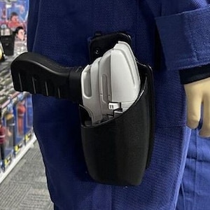 May include: A black holster with a white and gray gun inside. The holster is attached to a blue jumpsuit.
