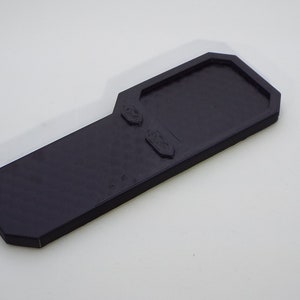 May include: A black plastic key-shaped object with a rectangular indentation on the top and two smaller indentations on the side.