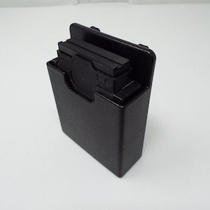 Peut inclure: Un étui rectangulaire noir avec une surface texturée. L'étui a un couvercle à charnière et un compartiment contenant plusieurs objets rectangulaires noirs. L'étui est posé sur un fond blanc.