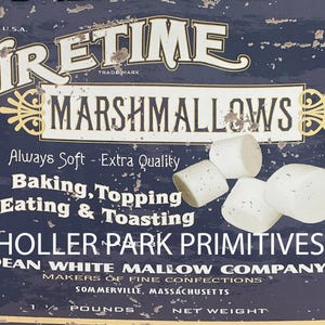 Könnte beinhalten: Ein Vintage-Blechschild, das für Firetime Marshmallows wirbt. Das Schild ist blau mit weißem Text und zeigt eine Grafik von Marshmallows. Der Text lautet "Firetime Marshmallows", "Immer weich - Extra Qualität", "Backen, Belegen, Essen & Toasten", "Holler Park Primitives", "Dean White Mallow Company", "Hersteller von feinen Süßwaren", "Somerville, Massachusetts", "1 1/2 Pfund", und "Nettogewicht".