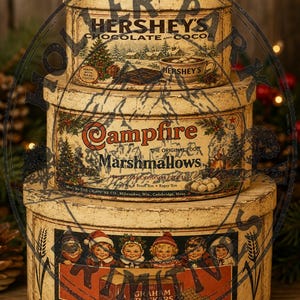 Könnte beinhalten: Ein Stapel aus drei runden, cremefarbenen Metalldosen im Vintage-Stil. Die oberste Dose zeigt das Hershey's-Branding und eine Winterszene. Die mittlere Dose trägt den Schriftzug Campfire Marshmallows. Die untere Dose zeigt eine Grafik mit Kindern.