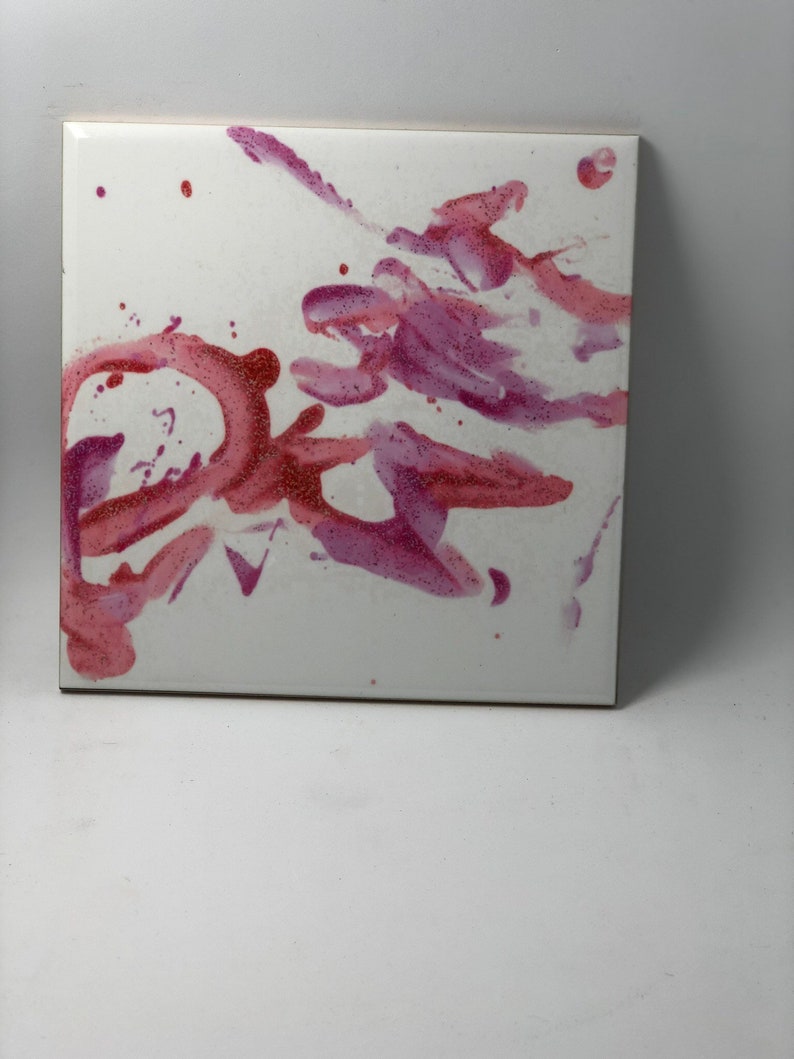 Puede incluir: Un azulejo de cer&aacute;mica blanco con salpicaduras abstractas de pintura rosa y roja. La pintura tiene una textura brillante.