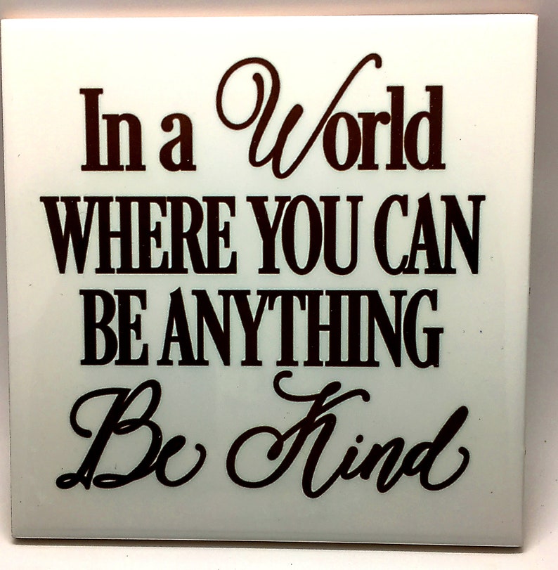 Puede incluir: Azulejo de cer&aacute;mica blanco con el texto "In a world where you can be anything Be Kind" en letras marrones.