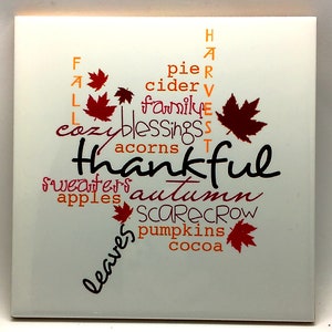 Puede incluir: Azulejo de cer&aacute;mica blanco con un dise&ntilde;o de arte de palabras con tem&aacute;tica oto&ntilde;al. Las palabras "Fall", "Thankful", "Autumn", "Sweaters", "Apples", "Leaves", "Pie", "Cider", "Family", "Blessings", "Acorns", "Scarecrow", "Pumpkins" y "Cocoa" est&aacute;n dispuestas en forma de hoja.