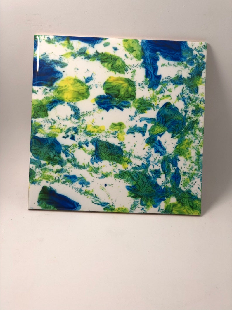 Puede incluir: Un azulejo de cer&aacute;mica cuadrado con fondo blanco y salpicaduras abstractas de pintura azul y verde.