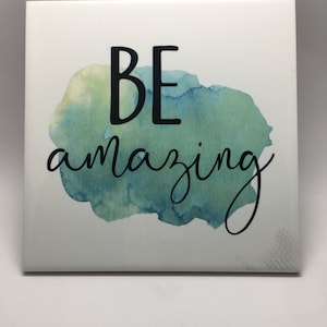 May include: White ceramic tile with a watercolor-style background in shades of green and yellow. The tile has the text "BE amazing" in black lettering.