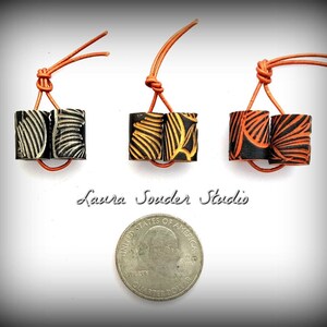 May include: Three pairs of black and orange polymer clay beads with a leaf pattern. Each pair is attached to a brown leather cord. A US quarter is included for size reference.