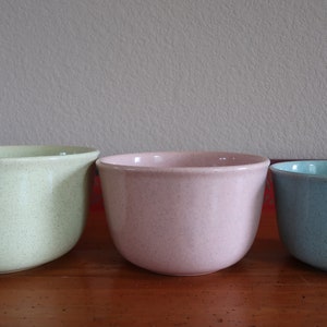 May include: Three ceramic bowls in different sizes and colors. The largest bowl is light green, the middle bowl is light pink, and the smallest bowl is light blue.