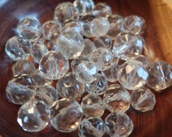 May include: A bowl filled with clear faceted glass beads. The beads are round and have a smooth, polished finish.