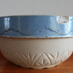 May include: A vintage white ceramic mixing bowl with a blue rim and a leaf pattern. The bowl has a chip on the rim.