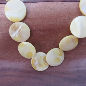 May include: A necklace made of round, yellow-toned, iridescent shell beads.