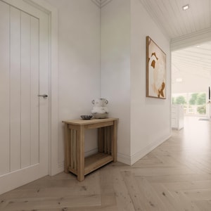 May include: Interior hallway with light wood flooring and white walls. A small wooden table with a decorative vase and bowl sits against the wall. An abstract painting hangs on the wall, and a door is on the left.