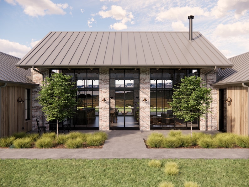 A rustic farmhouse made with reclaimed bricks in an alpine scene has large steel windows and doors on both sides. Snow capped mountains can be seen through the glazed living pavilion. The home features a metal roof with a chimney flue visible.