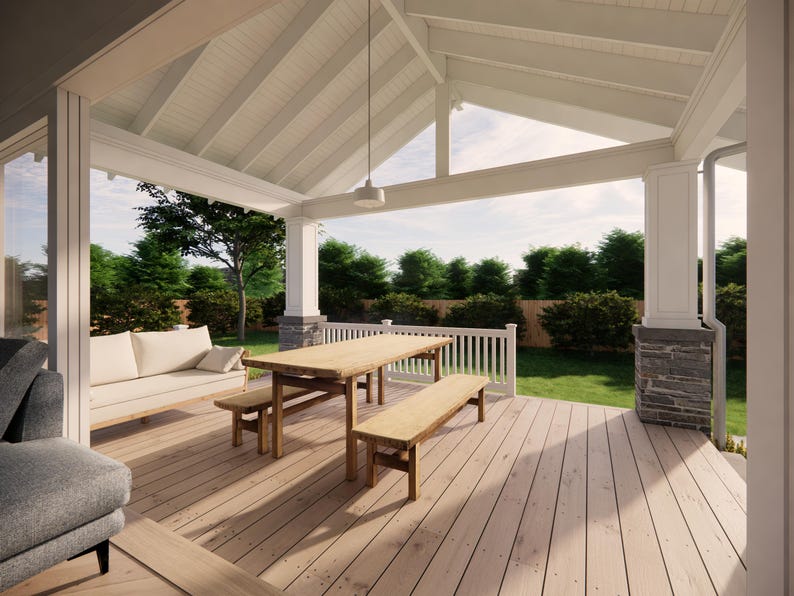 May include: A covered outdoor patio with a wooden deck, a wooden table, and benches. A white sofa with pillows is on the left. The patio has a white ceiling and columns. Green trees and grass are visible in the background.