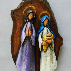 May include: A wooden cutout of the Holy Family, painted in a rustic style.  The figures are depicted in a traditional nativity scene, with Mary, Joseph, and the baby Jesus.  The background is a brown wood grain.