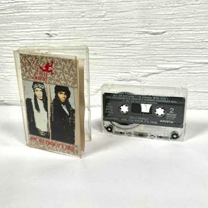 May include: Two Milli Vanilli cassette tapes in clear plastic cases. One case contains the album cover with two people. The other cassette tape has the text "Girl You Know It's True" and "Arista" printed on it.