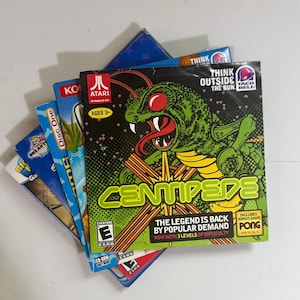 May include: A stack of five PC CD-ROM video game cases arranged in a fan shape. The top case features the Centipede game cover with a green insect illustration, the Atari logo, and text including Think Outside The Bun and Taco Bell branding.
